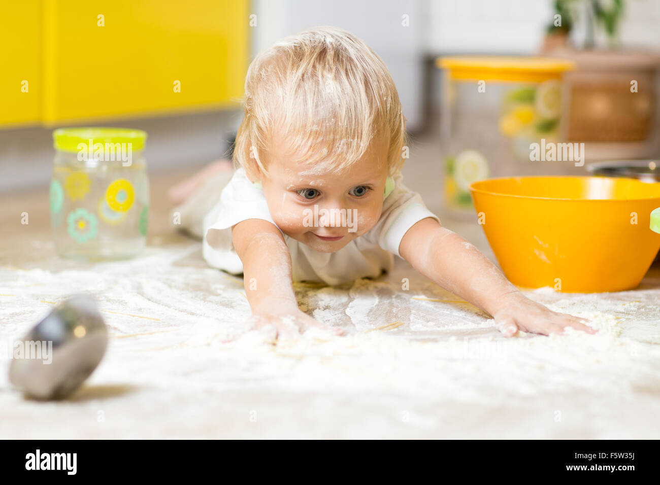 Bambino posa su disordinatissimi cucina, pavimento ricoperto di bianco di farina Foto Stock