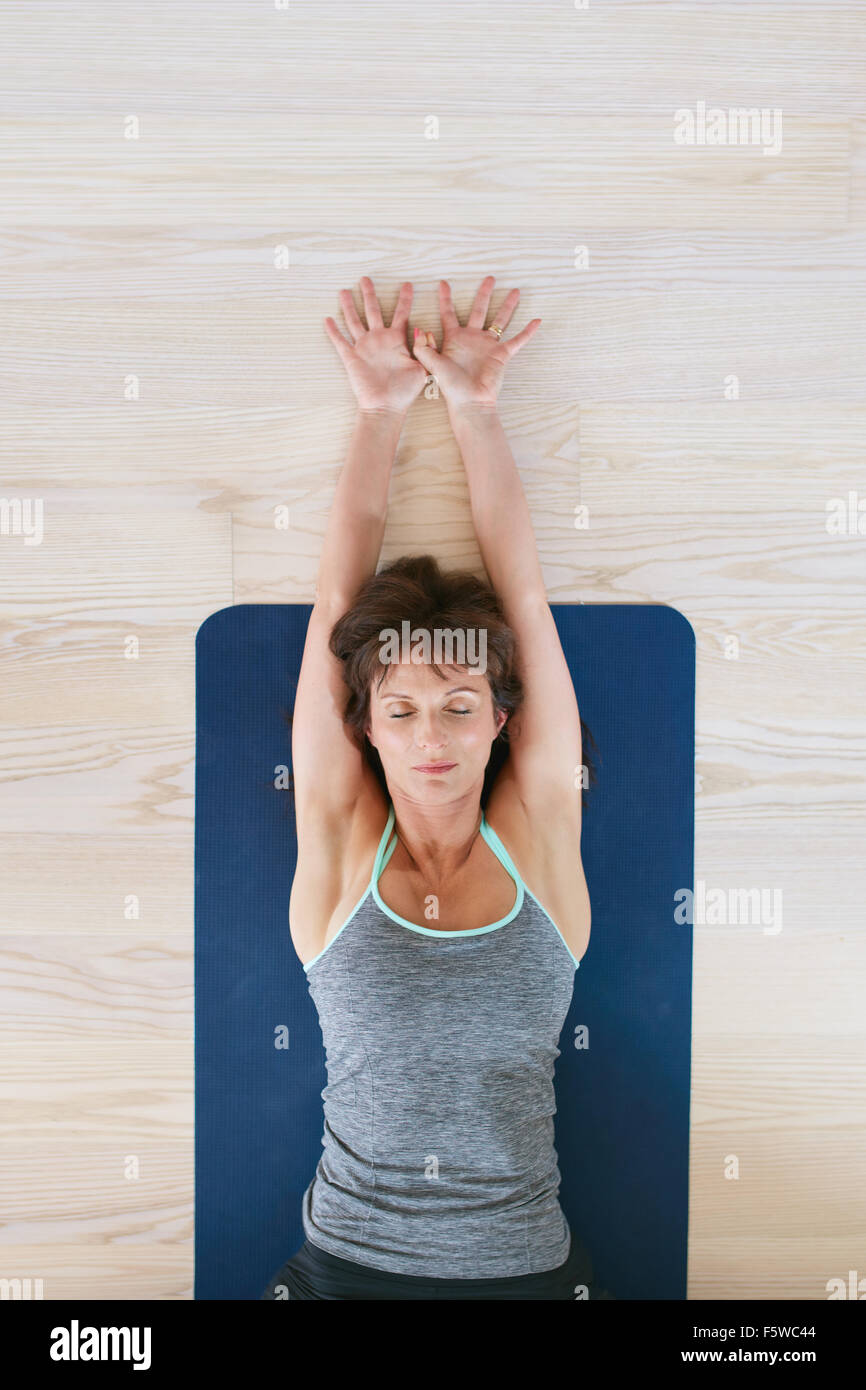 Vista superiore della donna sdraiata sul pavimento con gli occhi chiusi e distesa bracci. Donna Fitness esercita sul materassino yoga. Foto Stock
