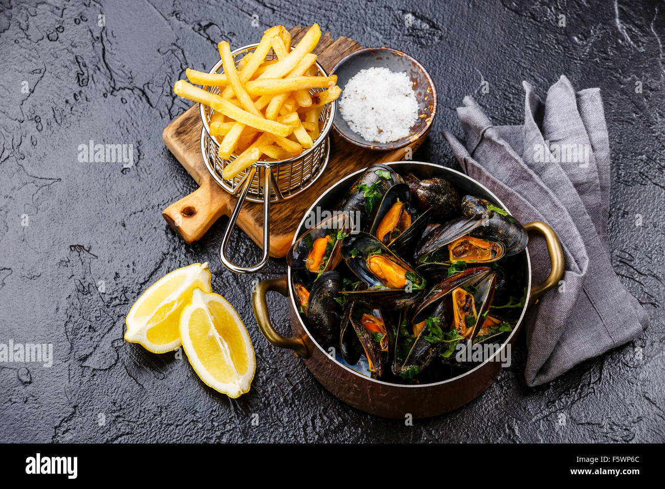 Le cozze in rame piatto di cottura e patatine fritte sulla pietra nera sullo sfondo Foto Stock
