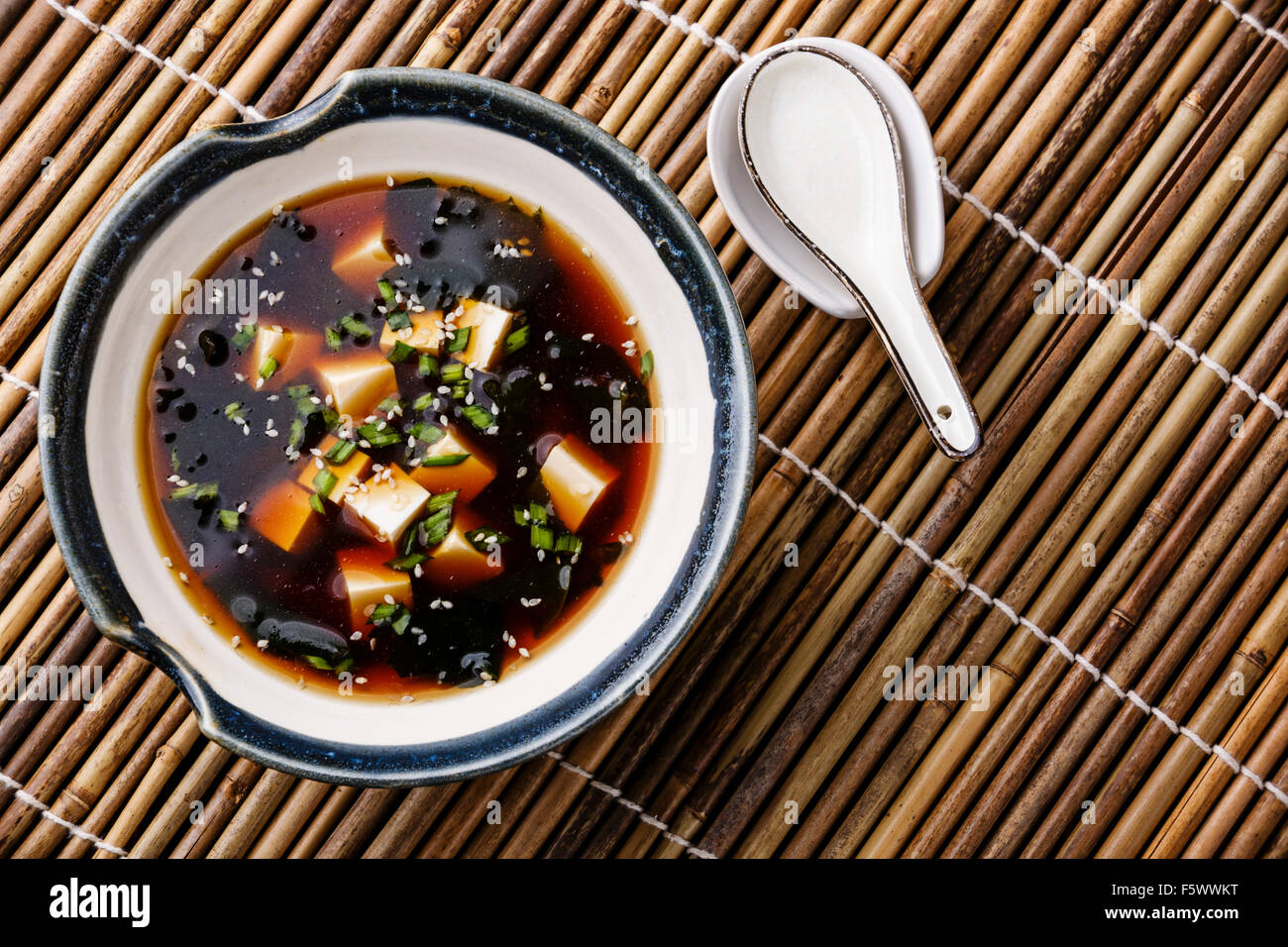 Zuppa di miso con tofu, alghe e sesamo in vaso su sfondo di bambù Foto Stock