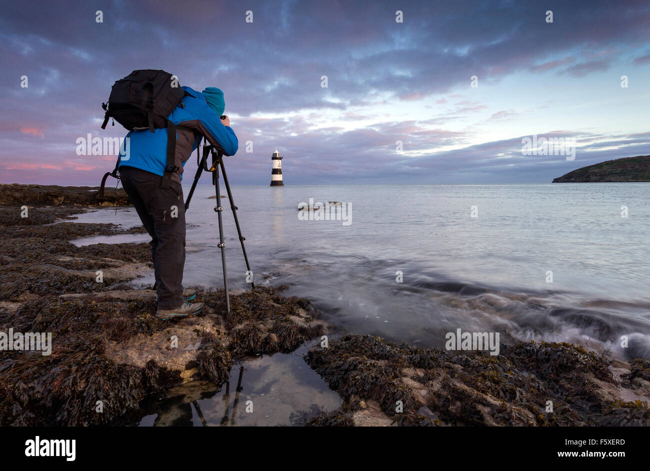 Fotografo in piedi sul litorale di fotografare un faro e seascape all'alba utilizzando un treppiede fotocamera montata Foto Stock