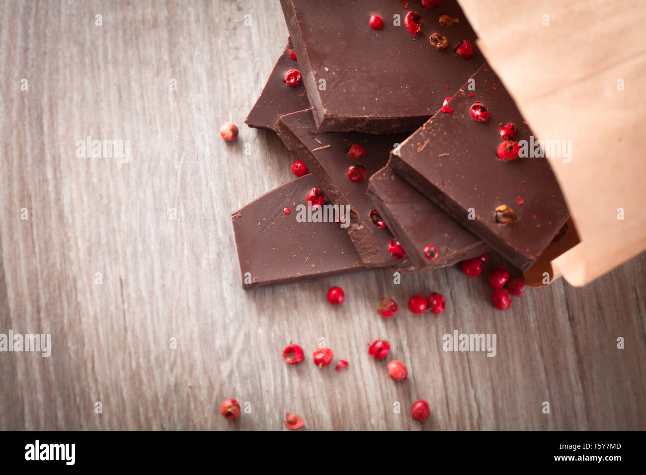 Pezzi di cioccolato fondente con pepe rosa sul tavolo Foto Stock
