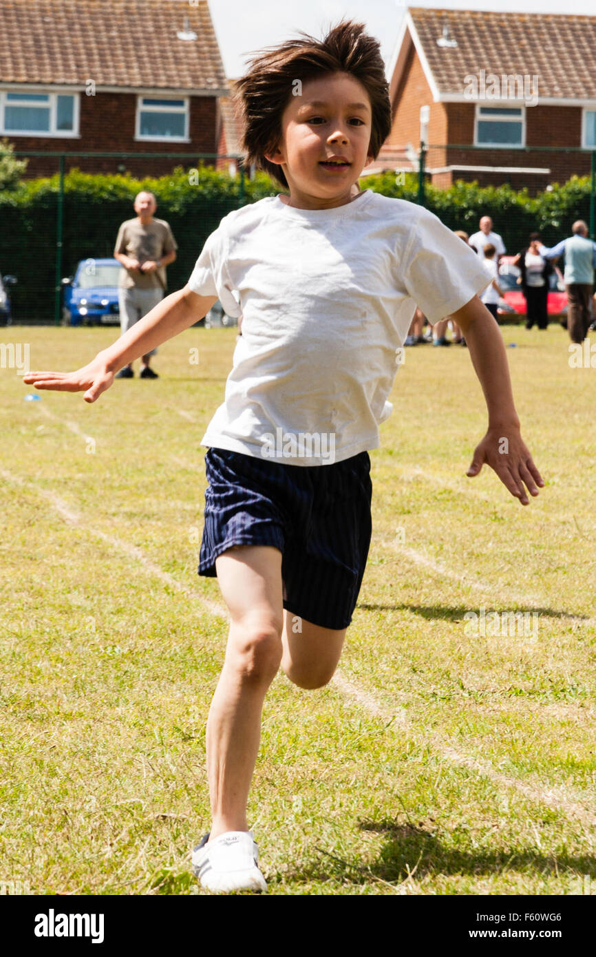 Bambino, ragazzo caucasico, 7-9 anni. All'aperto presso la scuola la giornata dello sport. In esecuzione su erba via verso viewer durante la gara. Eccitato espressione. Foto Stock