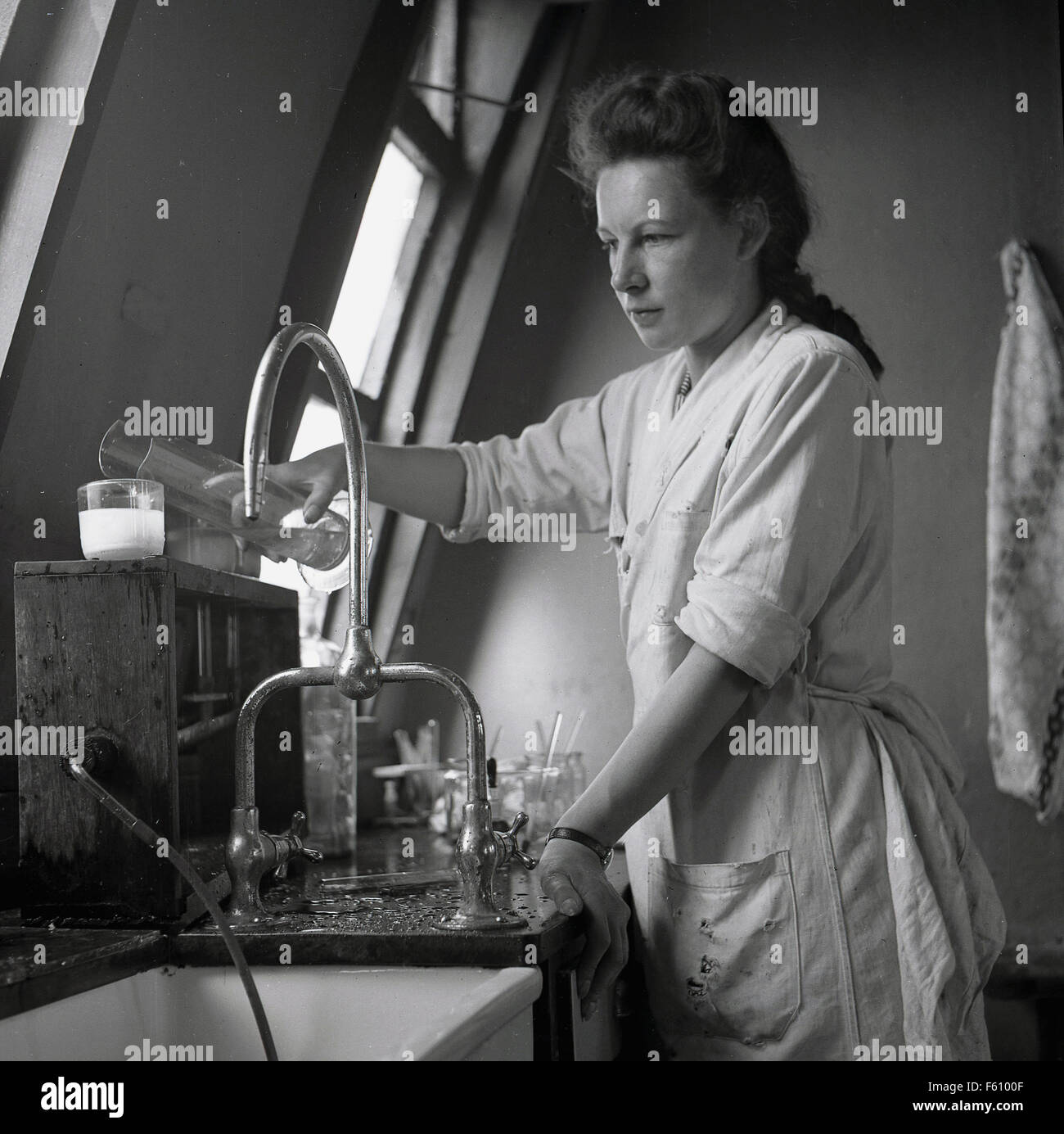 Anni Cinquanta foto storiche, rivestito bianco giovane donna adulto studente facendo un esperimento chimico in un piccolo piano superiore laboratorio. Foto Stock