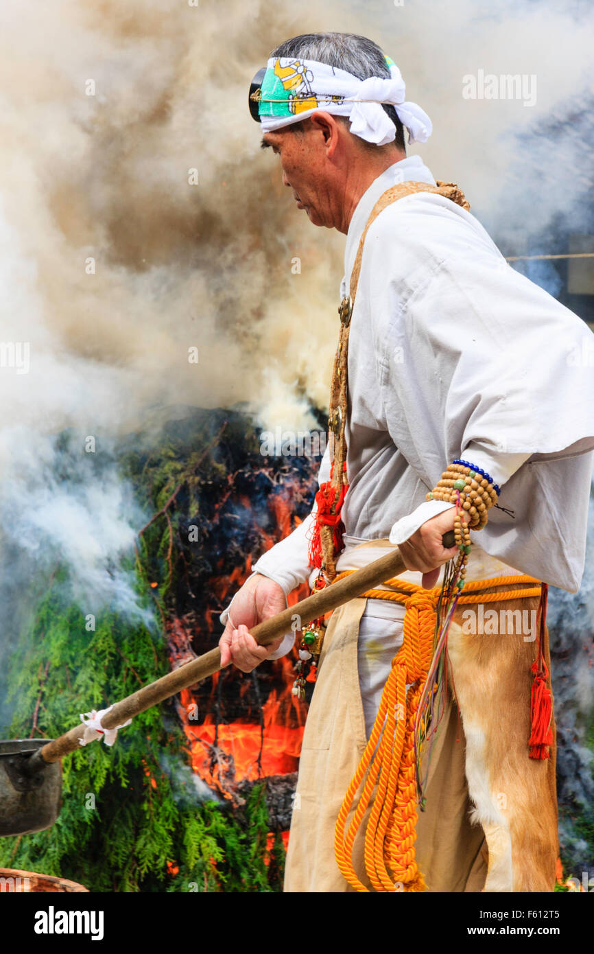 Giappone, Nishinomiya, Mondo Yakuji tempio. Sacerdote in costume yamabushi ladling tazze di paura di acqua su fumatori falò rituale durante la cerimonia mensile. Foto Stock