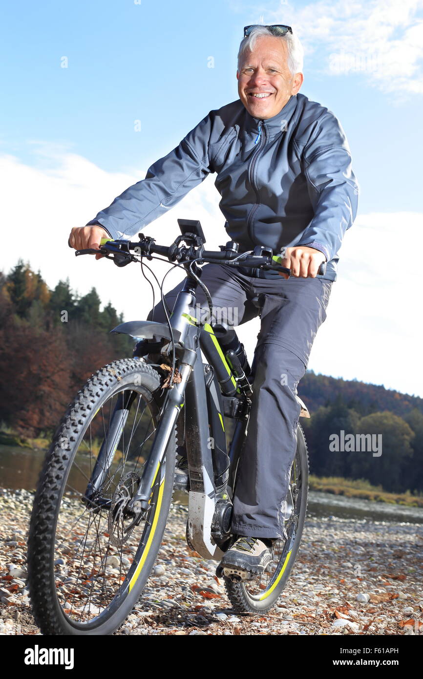 Un Senior sull'e-mountain bike su un fiume Foto Stock