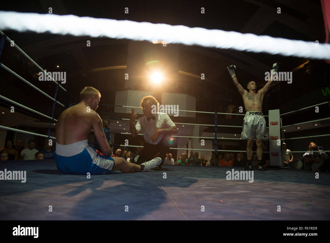 Un boxer pro è stato abbattuto e ha un conteggio di arbitro, Victor con "power" scritto sul suo shorts solleva le braccia Foto Stock