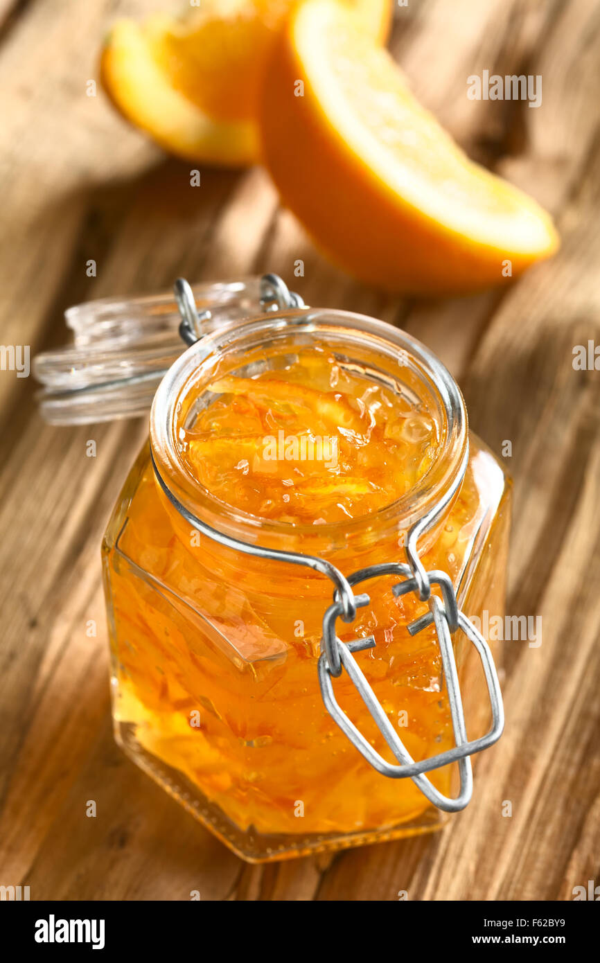 Orange jam swing-top jar sul legno con fettine di arancia in retro, fotografati con luce naturale (messa a fuoco selettiva) Foto Stock