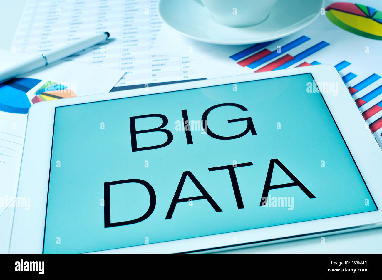 Il testo big dati nella schermata di un tablet su un tavolo pieno di grafici e fogli di calcolo e con una tazza di caffè o di tè Foto Stock