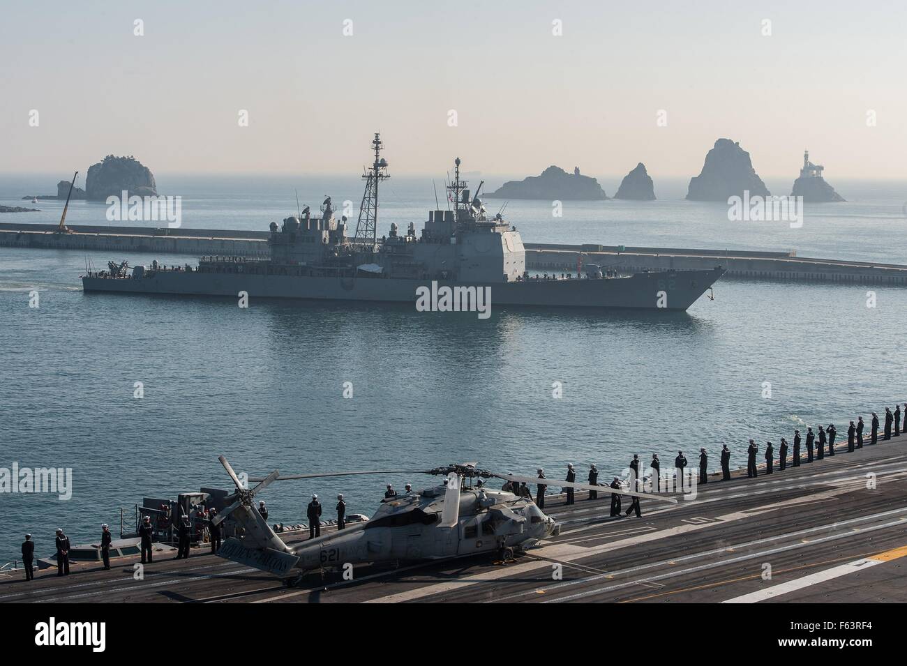 Gli Stati Uniti I marinai della marina stand al resto parata mentre manning le rotaie a bordo della Nimitz-classe-nucleare powered supercarrier USS Ronald Reagan a fianco della Ticonderoga-class guidato-missili cruiser USS Chancellorsville come essi partono il porto di Busan dopo un avviamento visita porta Novembre 4, 2015 a Busan, in Corea del Sud. Foto Stock