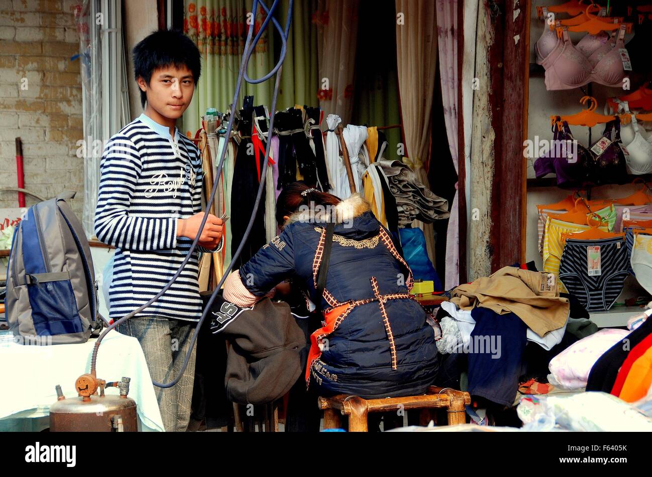 Il jiu Chi Town, Cina - 1 Dicembre 2007: la donna che lavora in una macchina da cucire nel suo negozio di sartoria e suo figlio adolescente Foto Stock