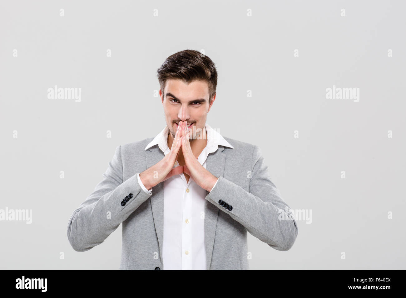 Sorridente giovane uomo in giacca grigia e camicia bianca mani piegate Foto Stock