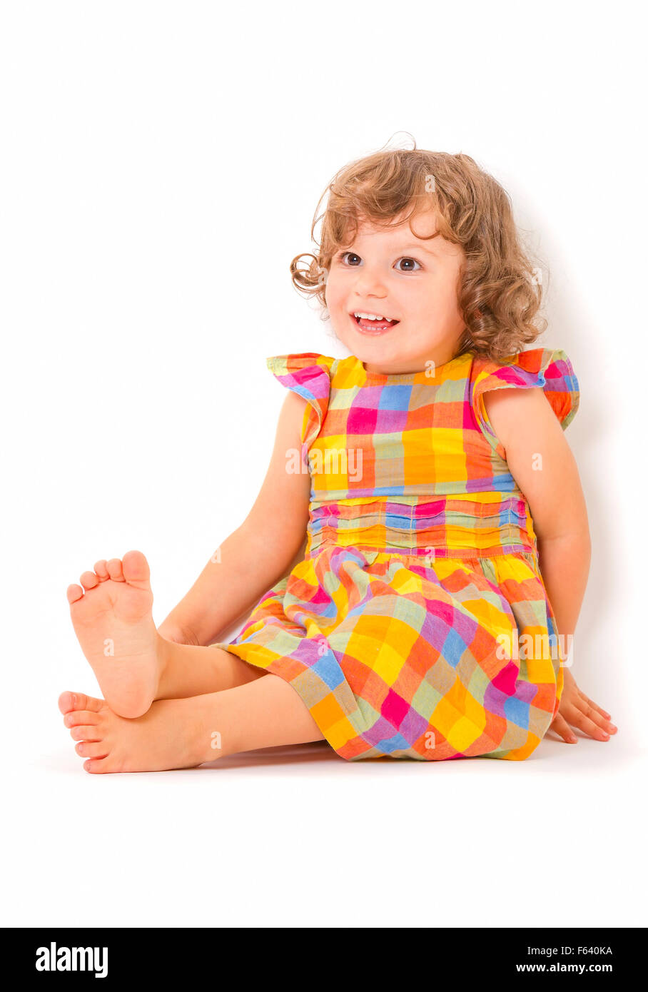 Incantevole piccola ragazza seduta sul pavimento e sorridente su sfondo bianco. Foto Stock