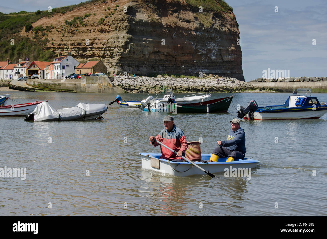 Soleggiata giornata estiva, 2 i pescatori sono il canottaggio a riva in una piccola barca con loro la pesca di cattura - porto di mare, Staithes' village, North Yorkshire, Regno Unito. Foto Stock