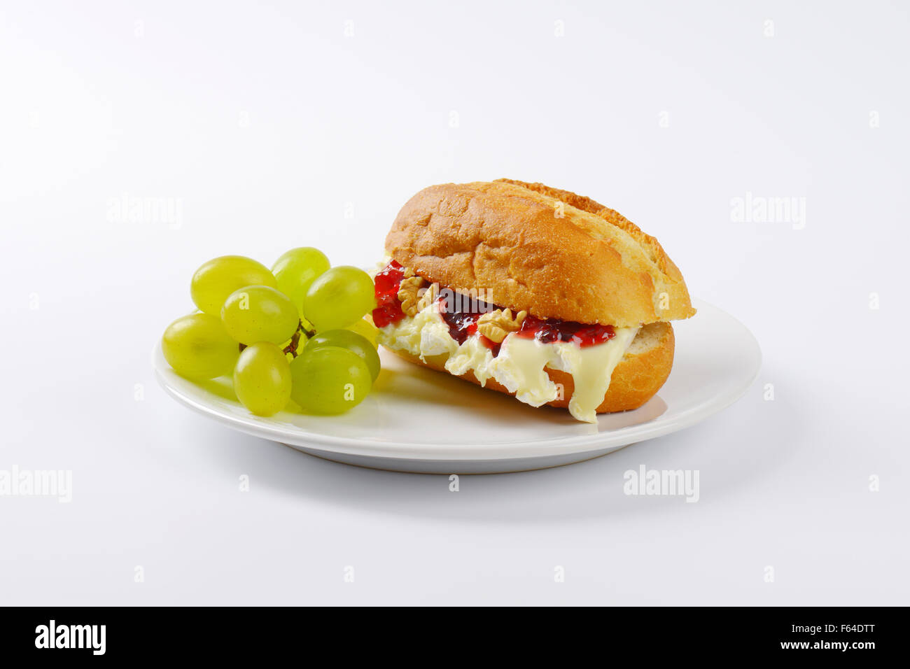 Piccola baguette con formaggio brie, noci, marmellata e uva sulla piastra bianca Foto Stock