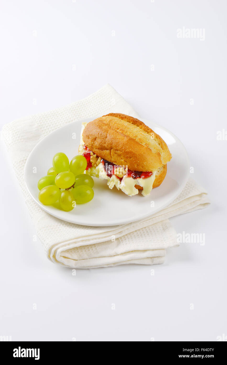 Piccola baguette con formaggio brie, noci, marmellata e uva sulla piastra bianca Foto Stock