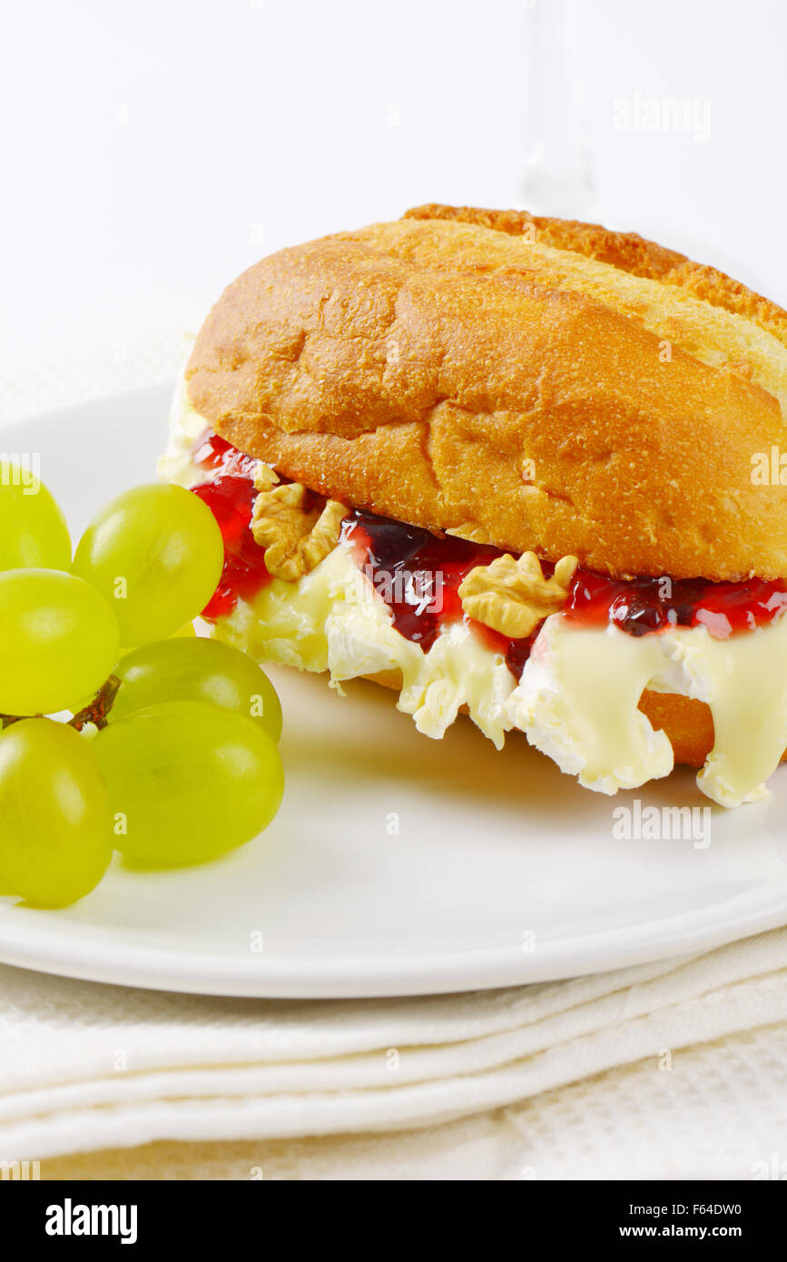 Piccola baguette con formaggio brie, noci, marmellata e uva sulla piastra bianca Foto Stock
