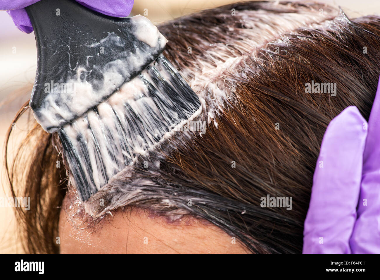 Parrucchiere di applicare un colore al marrone capelli di una femmina di client in un salone con un pennello applicatore, vista ravvicinata Foto Stock