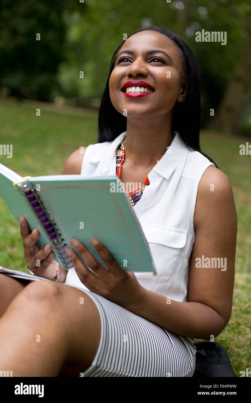 Studente seduto nel parco mentre tiene il suo libro di testo Foto Stock