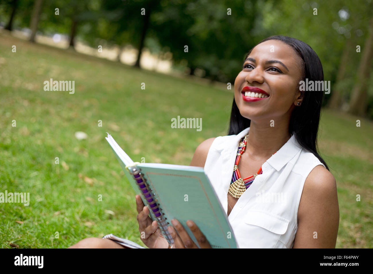 Giovane studente seduto nel parco mentre tiene il suo libro di testo Foto Stock