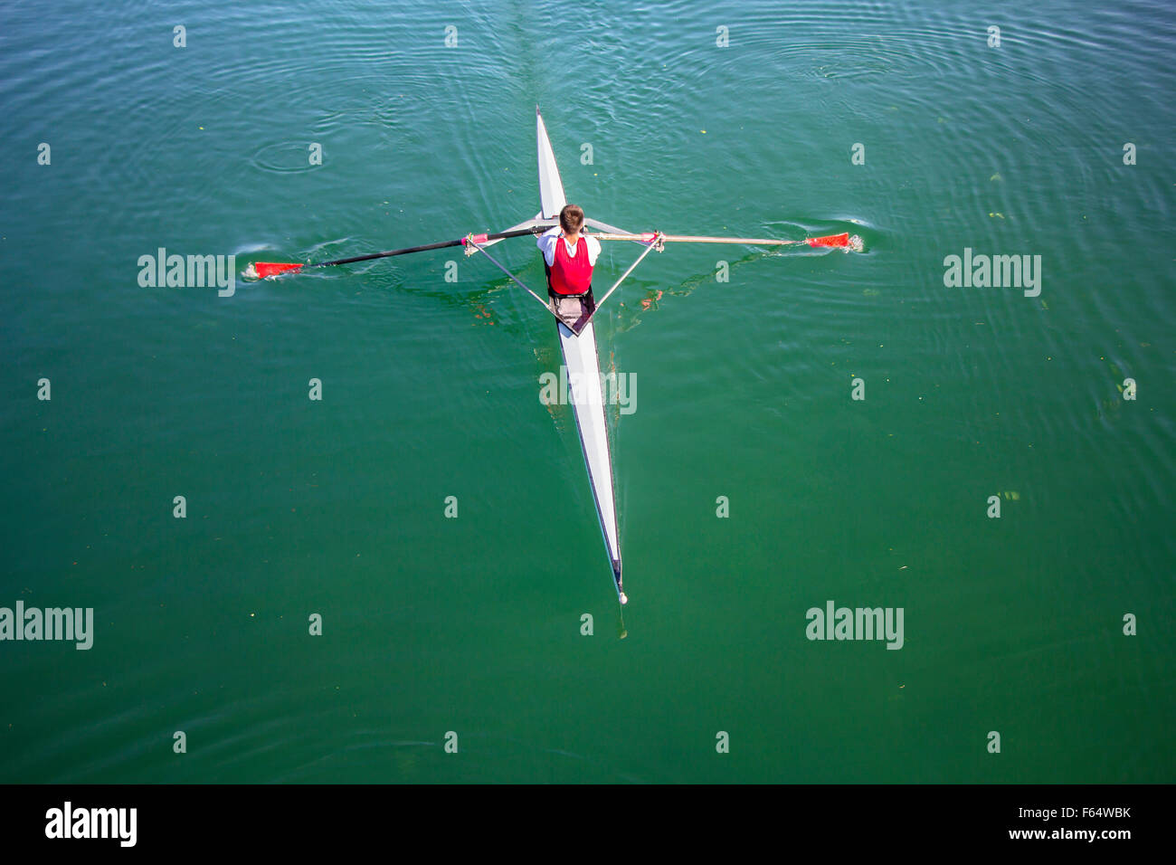 Giovane uomo vogatore in una barca, canottaggio sul lago tranquillo Foto Stock