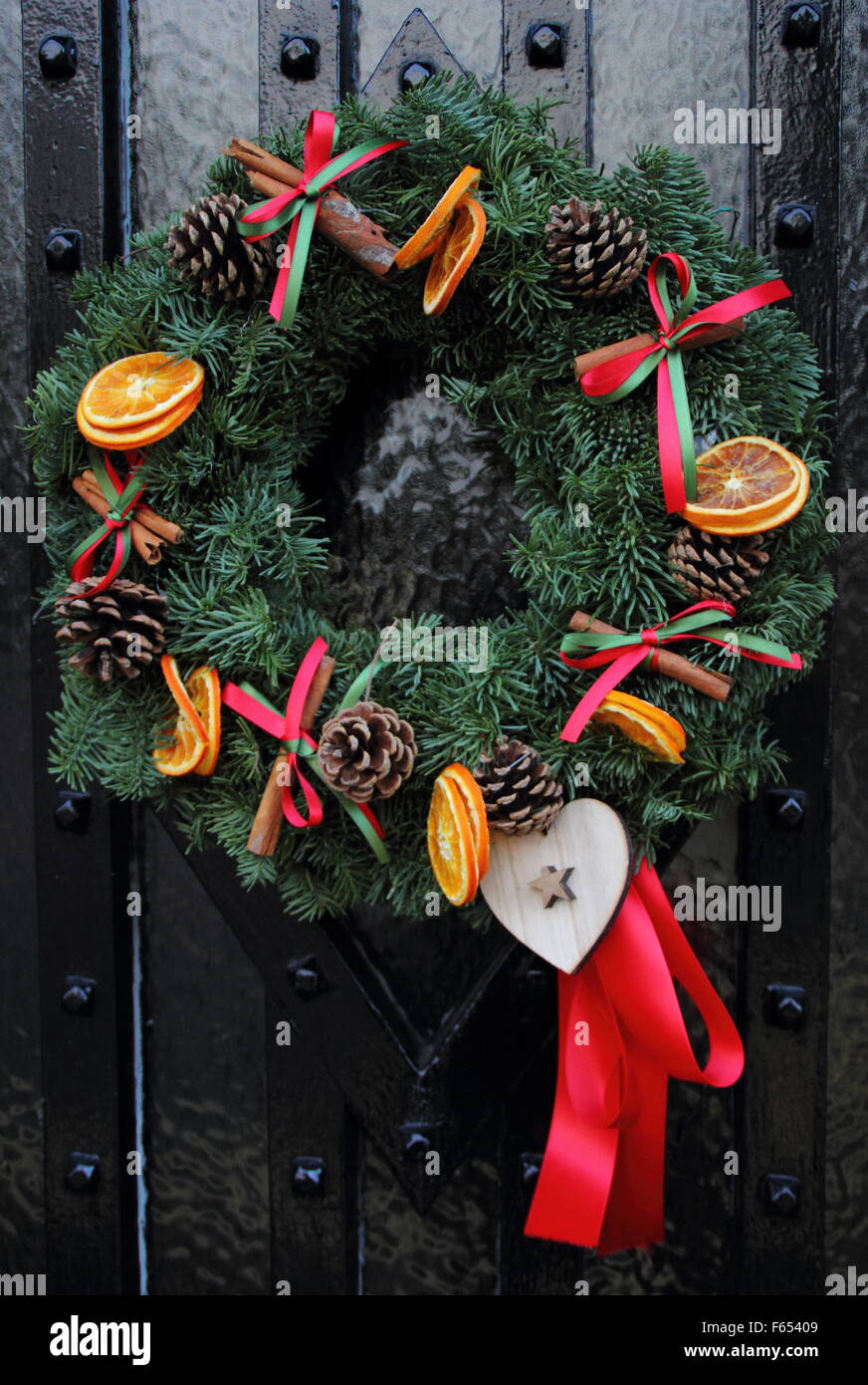 Una ghirlanda di Natale, o corona, essiccato con fettine di arancia e bastoncini di cannella appeso sulla porta di legno di un cottage di campagna Foto Stock