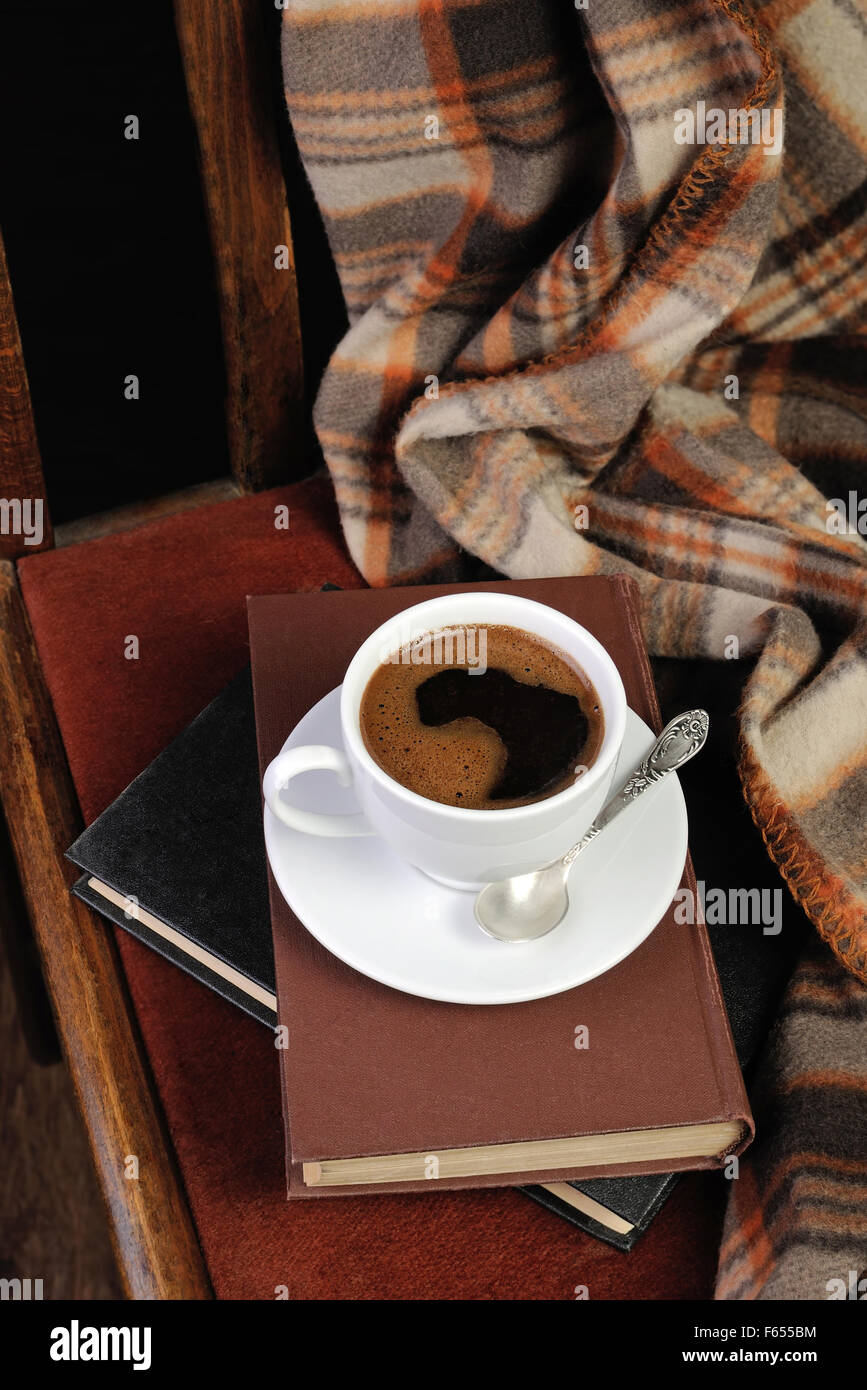 Tazza di caffè su una sedia con una pila di libri e una coperta Foto Stock