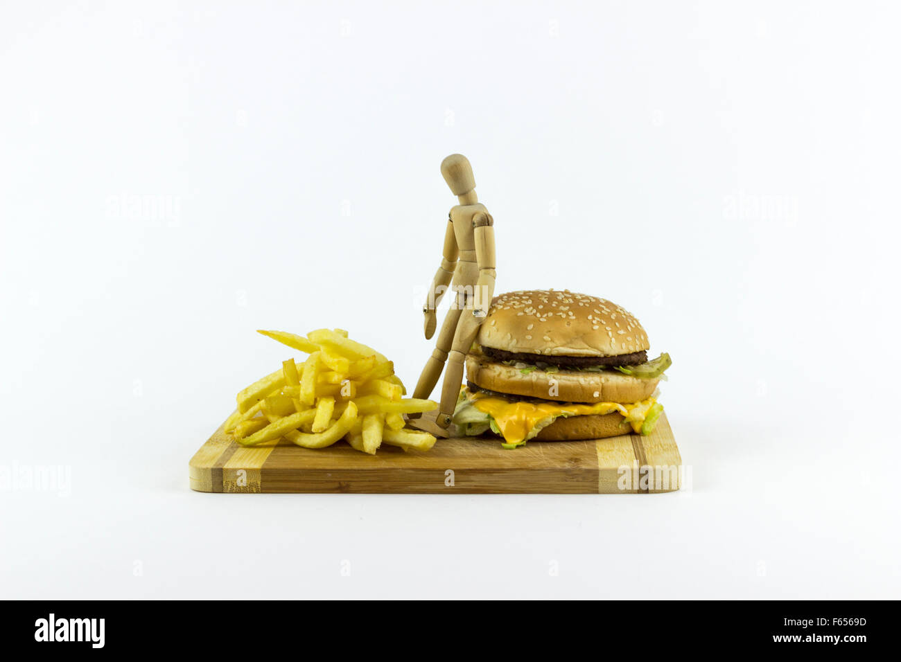 Il burattino di legno in piedi su un hamburger, guardando alcune patate fritte Foto Stock