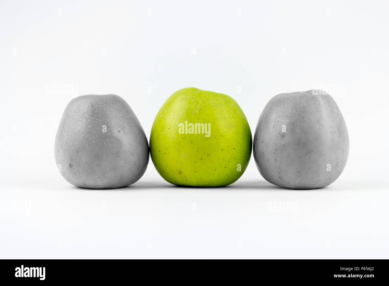 Tre mele verdi su sfondo bianco, medio uno dissaturato Foto Stock