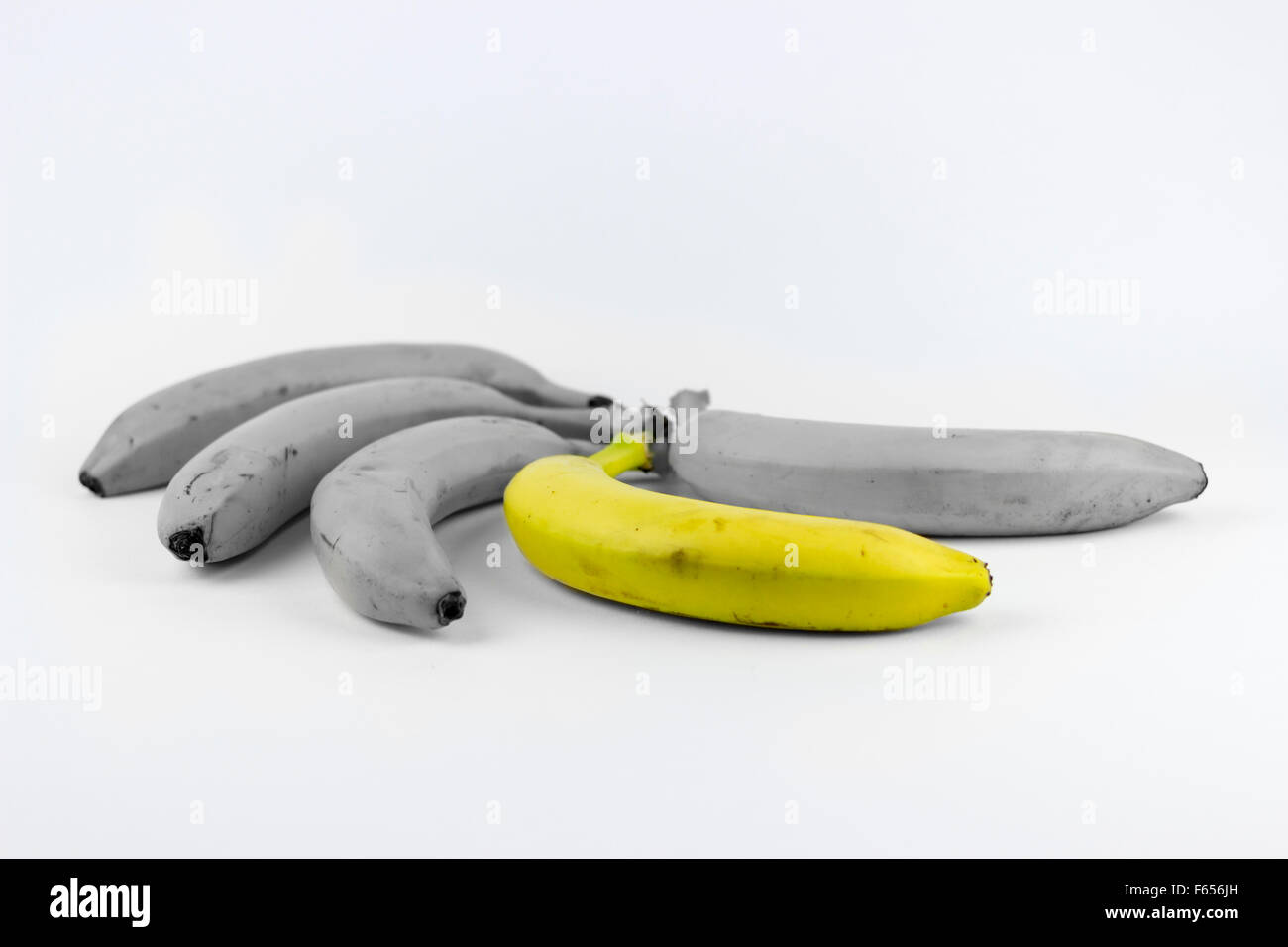 Cinque banane su uno sfondo bianco, con uno di loro dissaturato Foto Stock