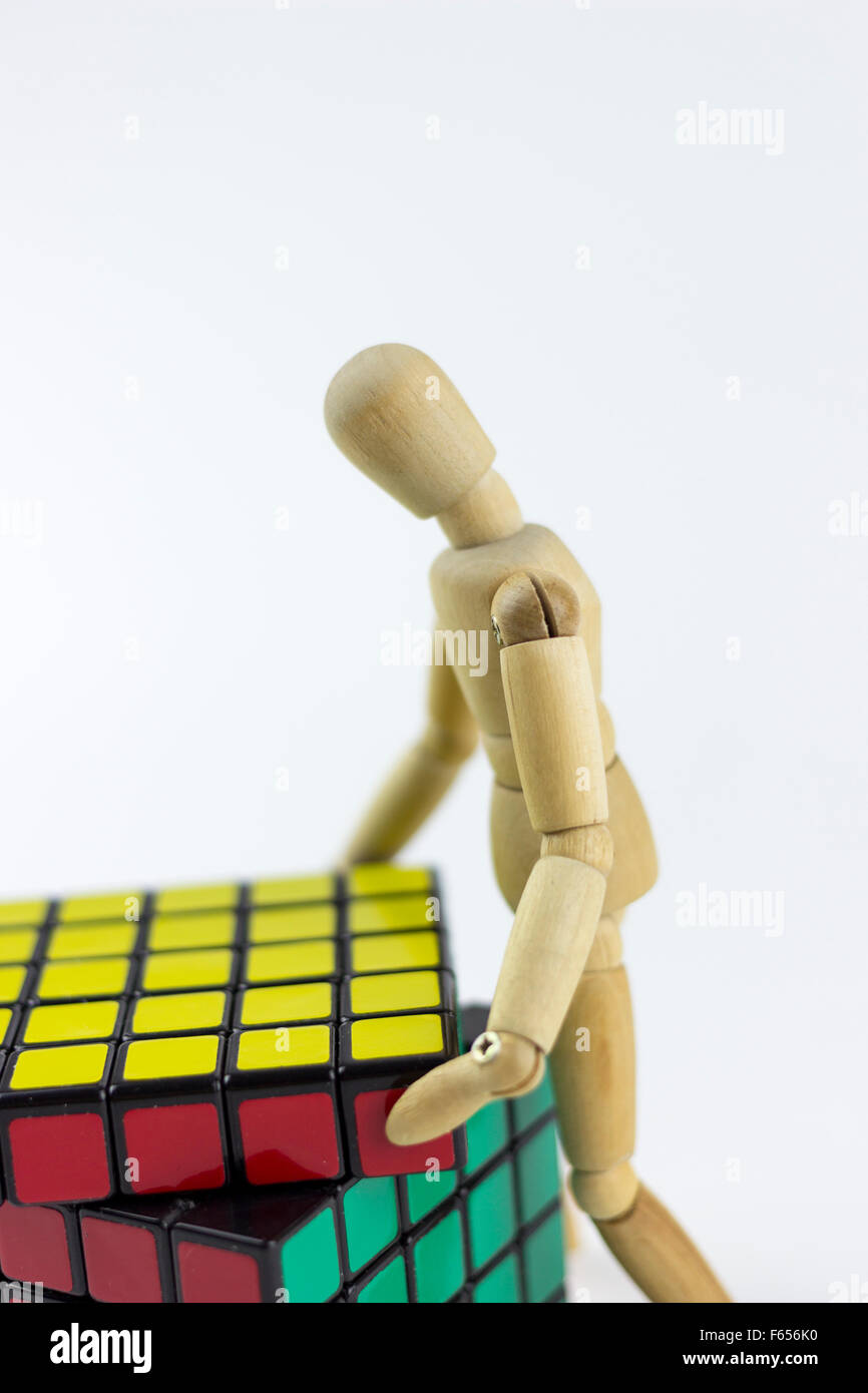 Legno Puppet cercando di risolvere un puzzle cubo, su sfondo bianco Foto Stock