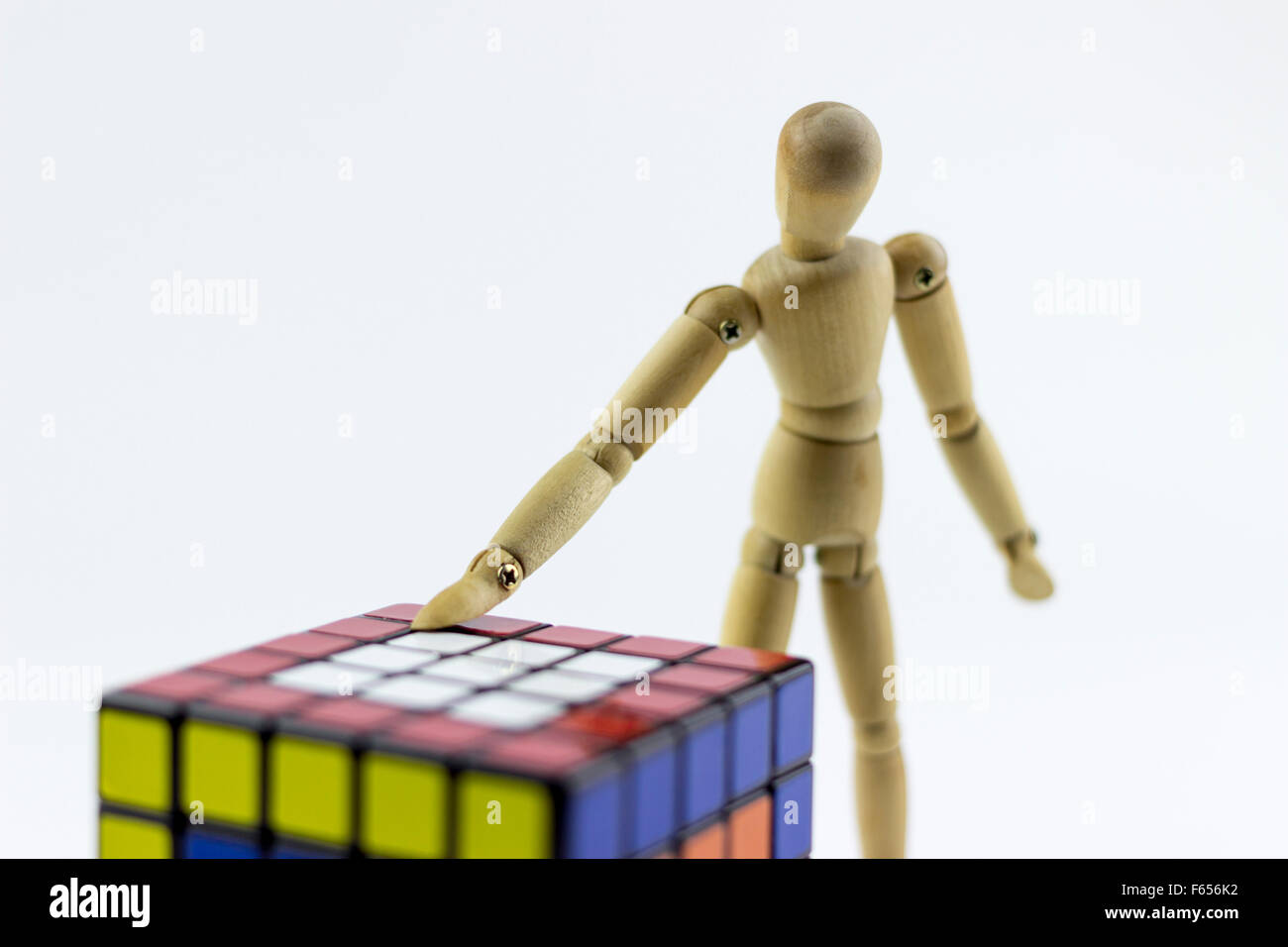 Legno Puppet cercando di risolvere un puzzle cubo, su sfondo bianco Foto Stock