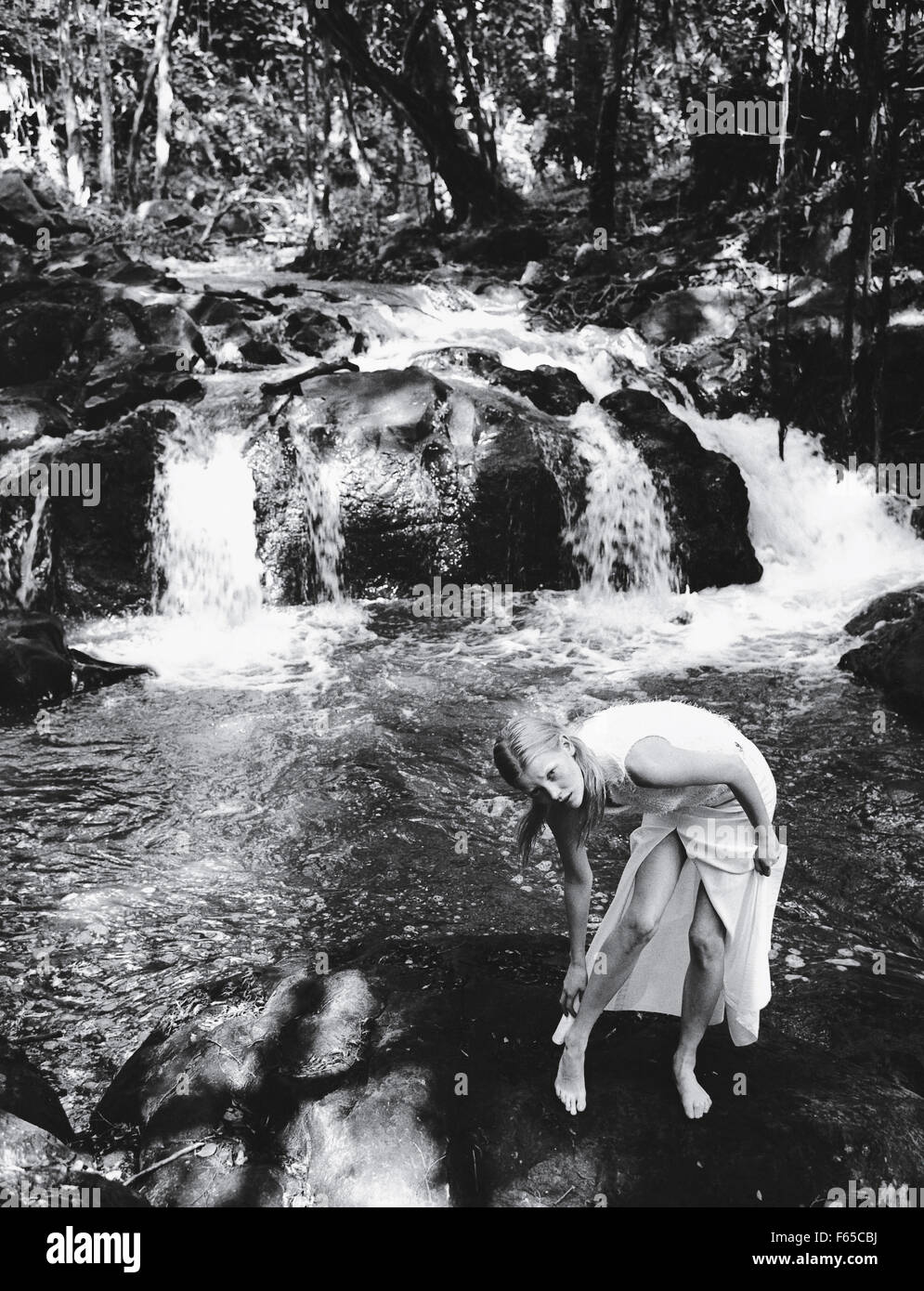 Donna bionda che indossa il vestito bianco in piedi di fronte a cascata, in bianco e nero Foto Stock