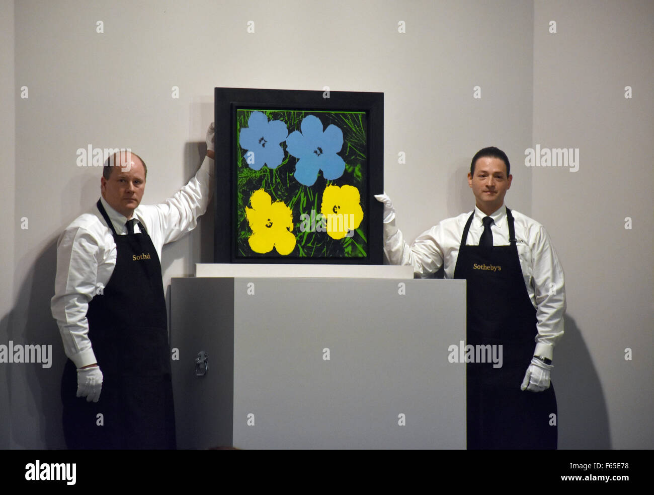 New York, Stati Uniti d'America. Xi Nov, 2015. Due dipendenti da Sotheby's auction house presente l'immagine 'fiori' da Andy Warhol a New York, Stati Uniti d'America, 11 novembre 2015. La foto è stata messa all'asta per 2,2 milioni di dollari, mantenendola al piolo in basso del valore stimato. Foto: CHRIS MELZER/dpa - nessun filo SERVICE -/dpa/Alamy Live News Foto Stock