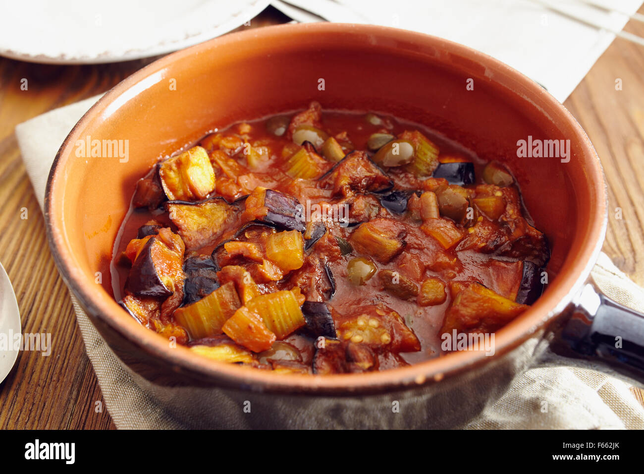 Caponata di melanzane, tradizionale piatto siciliano. Servita in un classico della coppa in ceramica su un tovagliolo su un vecchio tavolo di legno. Circondato Foto Stock Caponata di melanzane, tradizionale piatto siciliano. Servita in un classico della coppa in ceramica su un tovagliolo su un vecchio tavolo di legno. Circondato Foto Stock