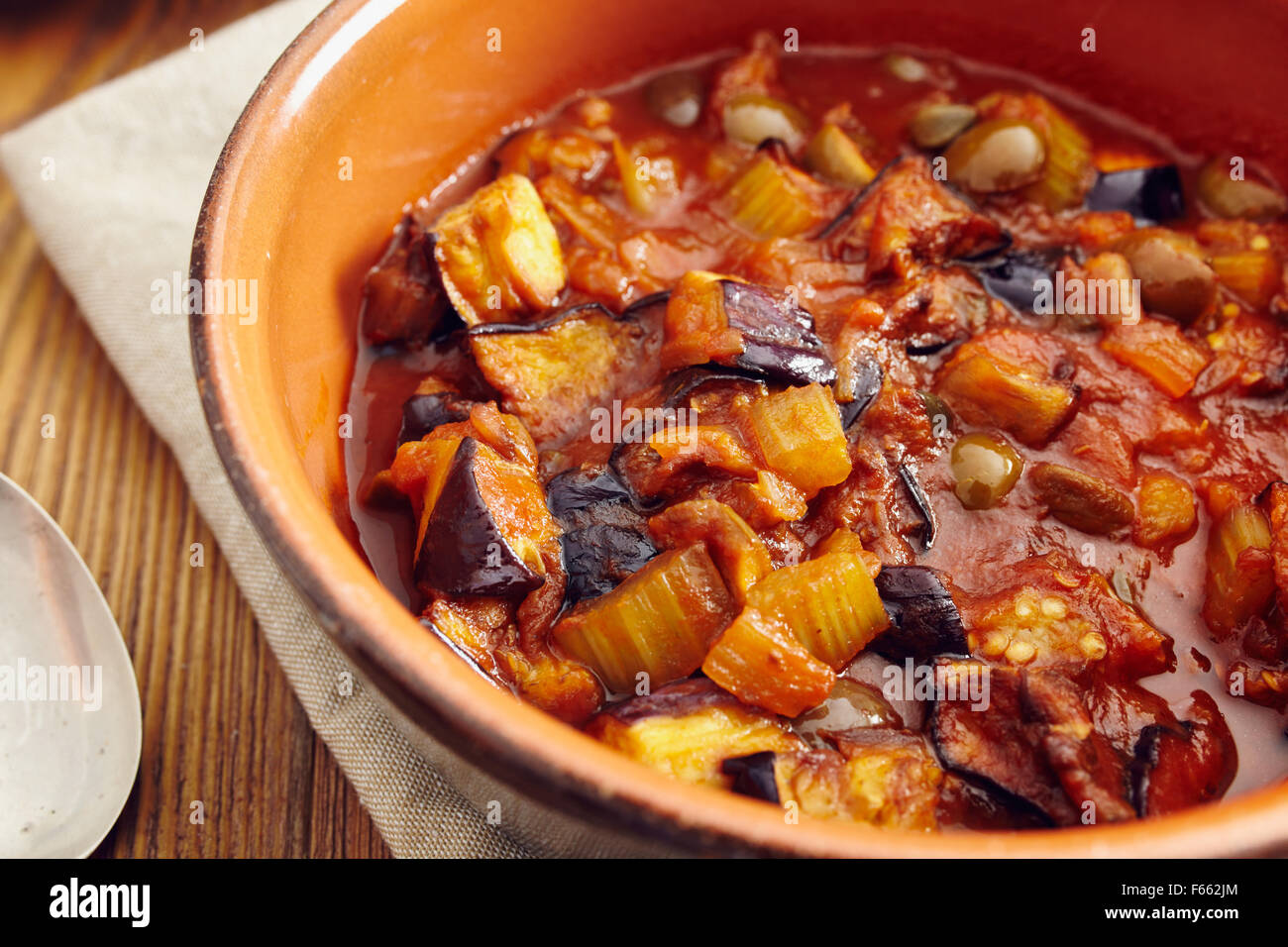 Caponata di melanzane, tradizionale piatto siciliano. Servita in un classico della coppa in ceramica su un tovagliolo su un vecchio tavolo di legno. Circondato Foto Stock Caponata di melanzane, tradizionale piatto siciliano. Servita in un classico della coppa in ceramica su un tovagliolo su un vecchio tavolo di legno. Circondato Foto Stock
