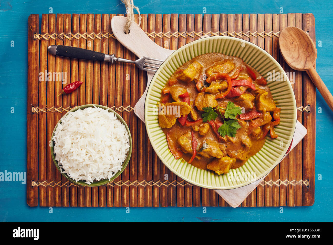 Curry maiale tritato in una ciotola con il riso basmati su un cartellone di bambù su un blu tavolo in legno Foto Stock