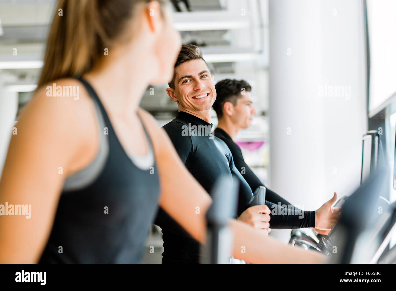 Uomo bello e giovane e bella donna che utilizza un motore passo-passo in una palestra e avere una conversazione Foto Stock