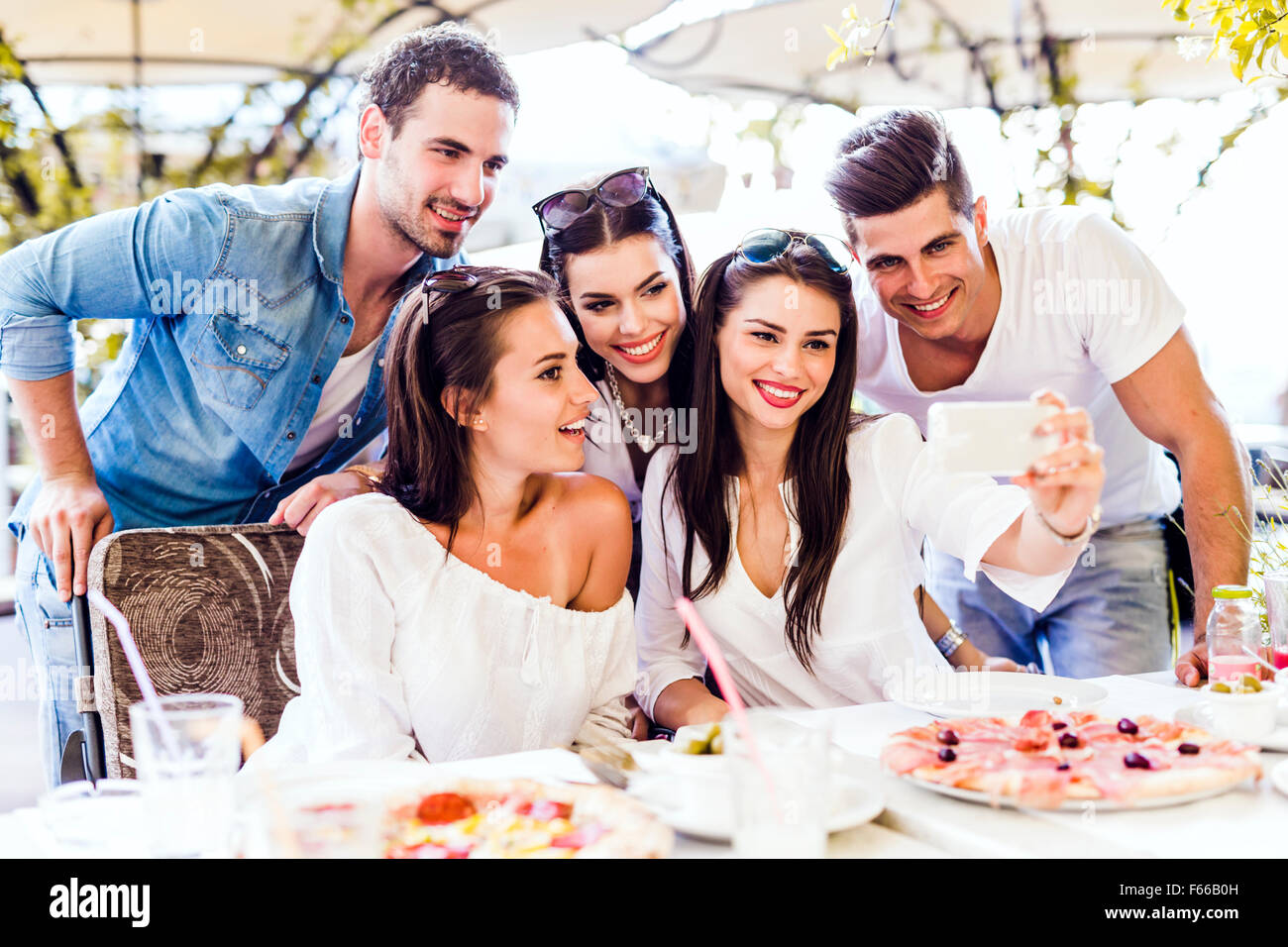 Un gruppo di giovani belle persone sedute in un ristorante e prendendo un selfie mentre sorridente Foto Stock
