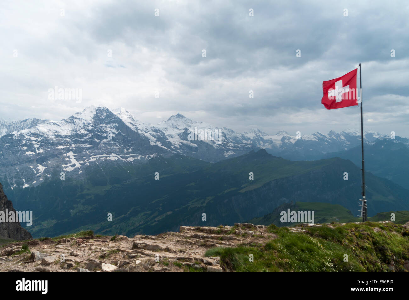 Bandiera svizzera volato in forte vento. Il maltempo, nuvole scure, pioggia. Sullo sfondo i monti Eiger, Mönch e Jungfrau montagne. Foto Stock