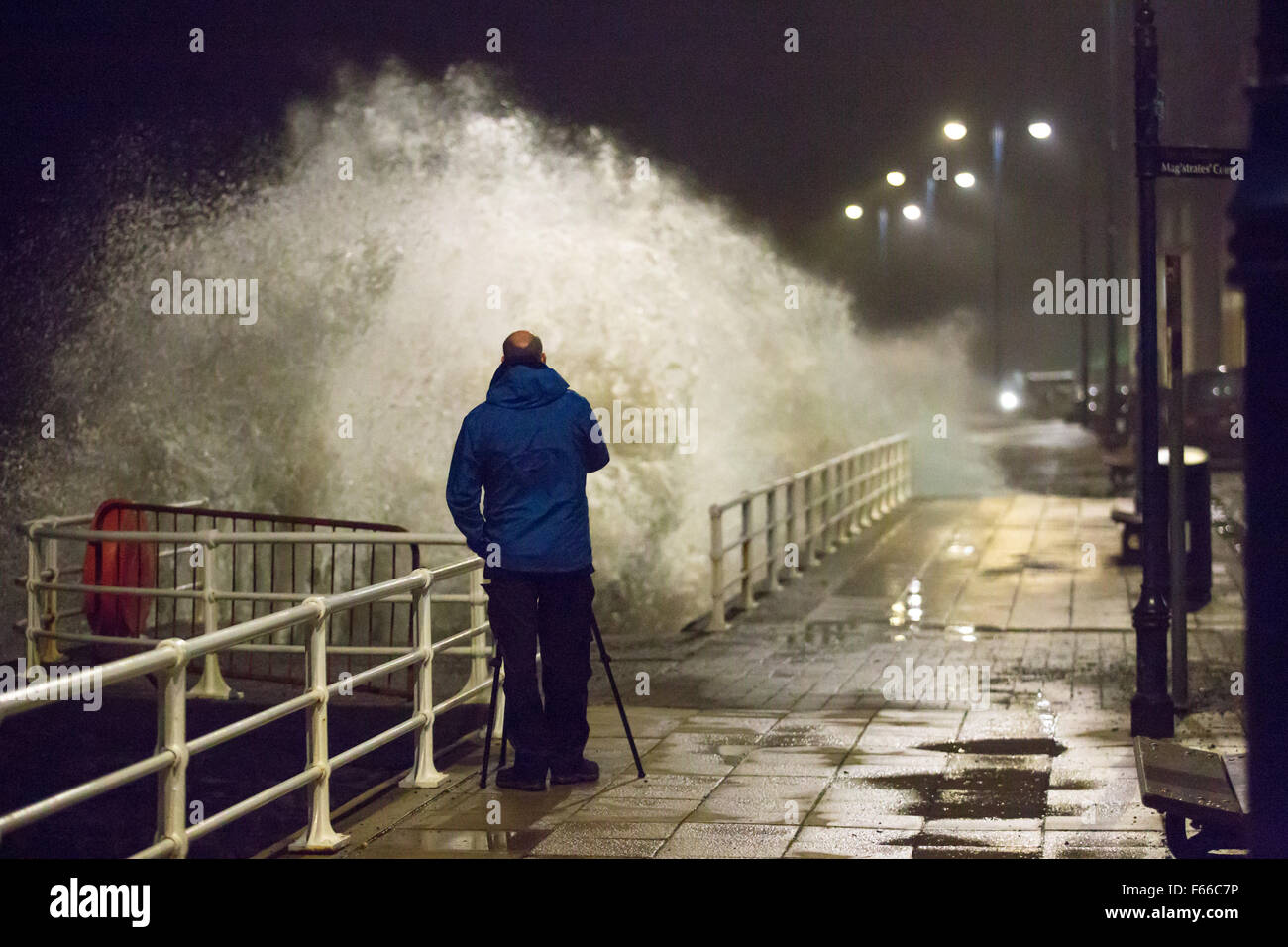 Aberystwyth, Wales, Regno Unito. 12 Nov 2015. Come tempesta Abigail hits Aberystwyth nel buio il forte vento e un alta marea si combinano per generare onde enormi. Un uomo prendendo fotografie come un'onda si blocca dietro di lui Credito: Alan Hale/Alamy Live News Foto Stock