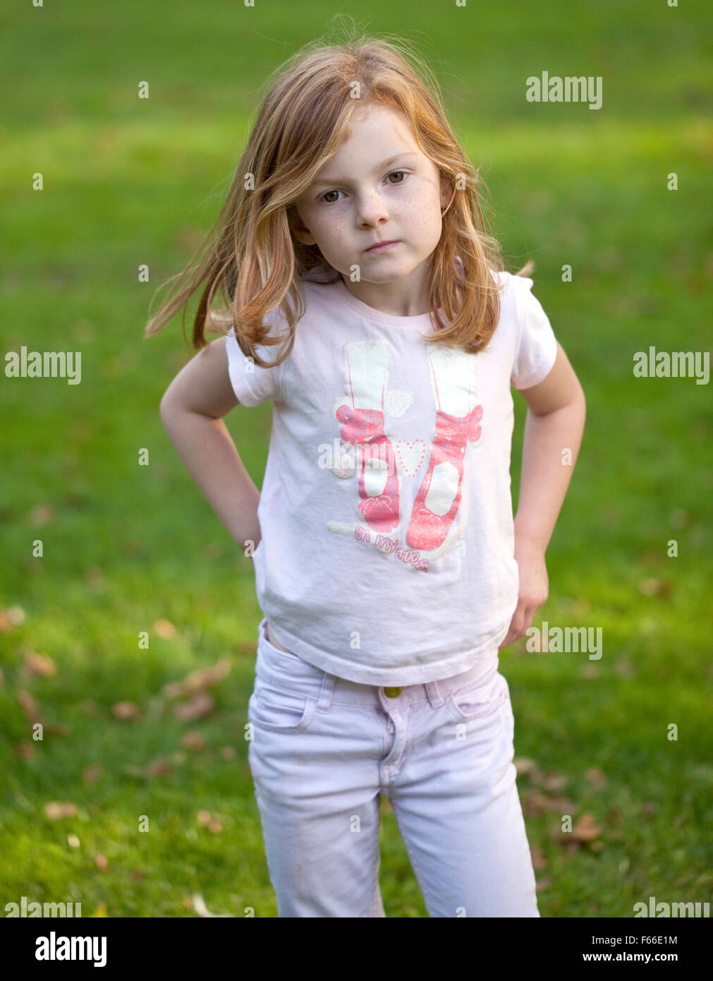 Una giovane ragazza con i capelli di zenzero che contrastano con il verde lussureggiante erba del parco, ha girato improvvisamente verso la telecamera. Foto Stock
