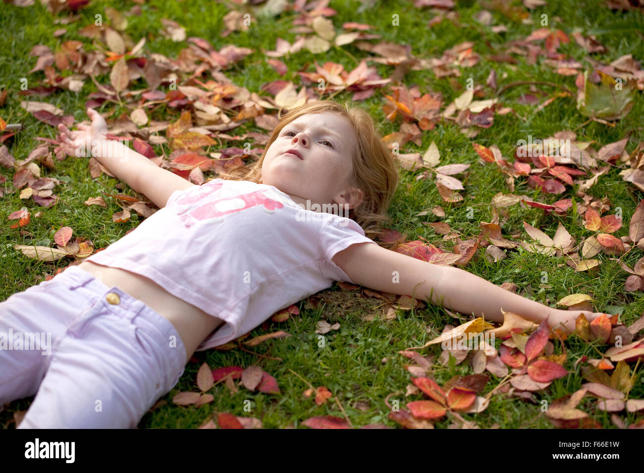 Una giovane ragazza, cercando piuttosto stufi, sdraiato su alcune foglie di autunno. Foto Stock