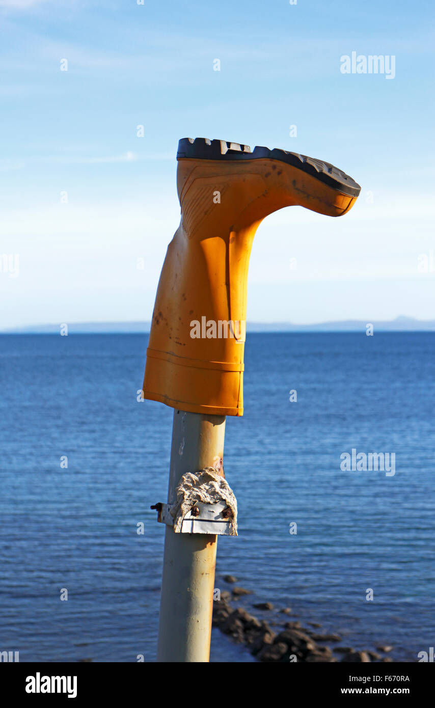 Una sola gomma gialla boot posizionato capovolto su un palo di legno. Foto Stock