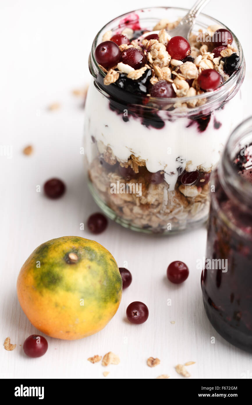 Il Granola di mirtillo palustre di confettura di mirtilli parfait di prima colazione. Farina di avena snack con muesli, frutti di bosco freschi, yogurt in un vasetto di vetro su bianco woo Foto Stock