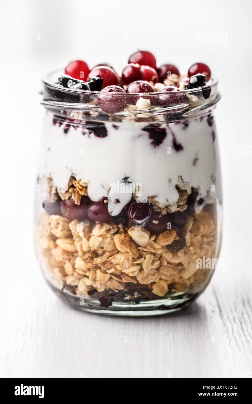 Il Granola di mirtillo palustre di confettura di mirtilli parfait di prima colazione. Farina di avena snack con muesli, frutti di bosco freschi, yogurt in un vasetto di vetro su bianco woo Foto Stock