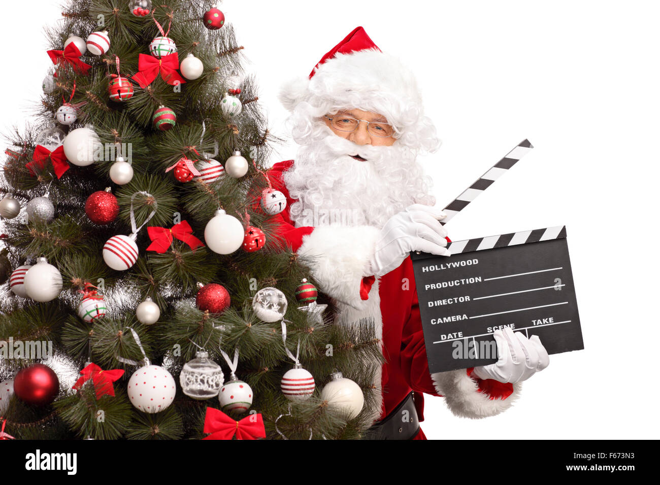 Santa Claus in posa dietro a un albero di Natale e tenendo un filmato clapperboard isolati su sfondo bianco Foto Stock