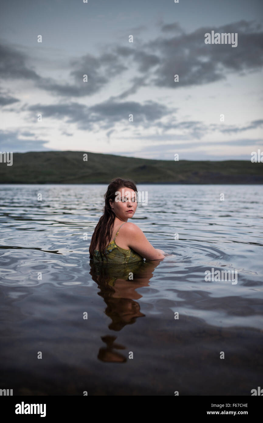 Dreaming: una giovane donna femmina ragazza seduta da sola con gli occhi chiusi in un lago Foto Stock