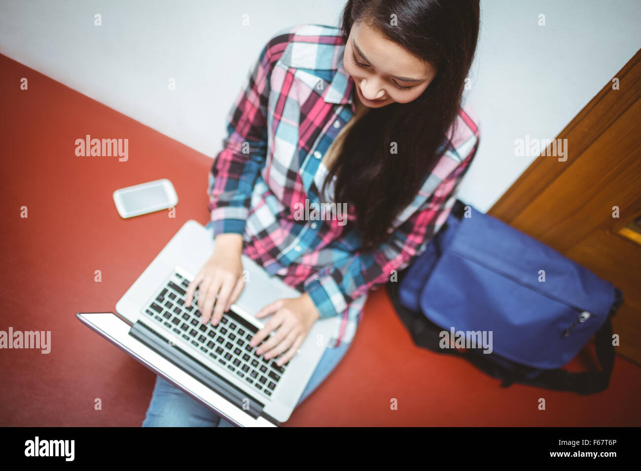 Sorridente studente seduto sul pavimento e utilizzo di computer portatile Foto Stock
