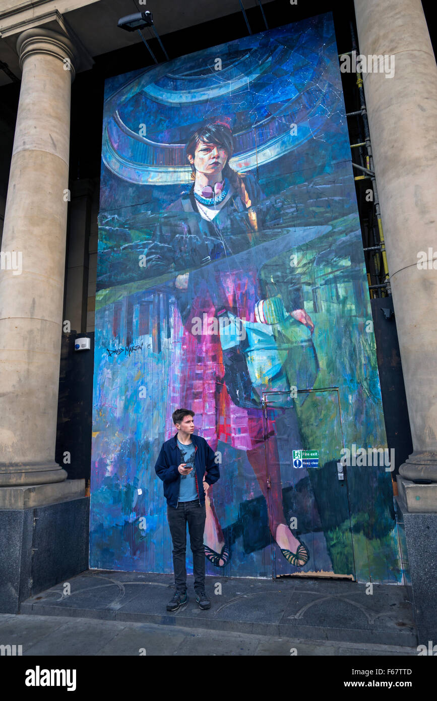 Un giovane uomo attende da un pezzo di arte di strada da David Martin in un edificio rinnovato in St Andrew Square, Edimburgo. Foto Stock